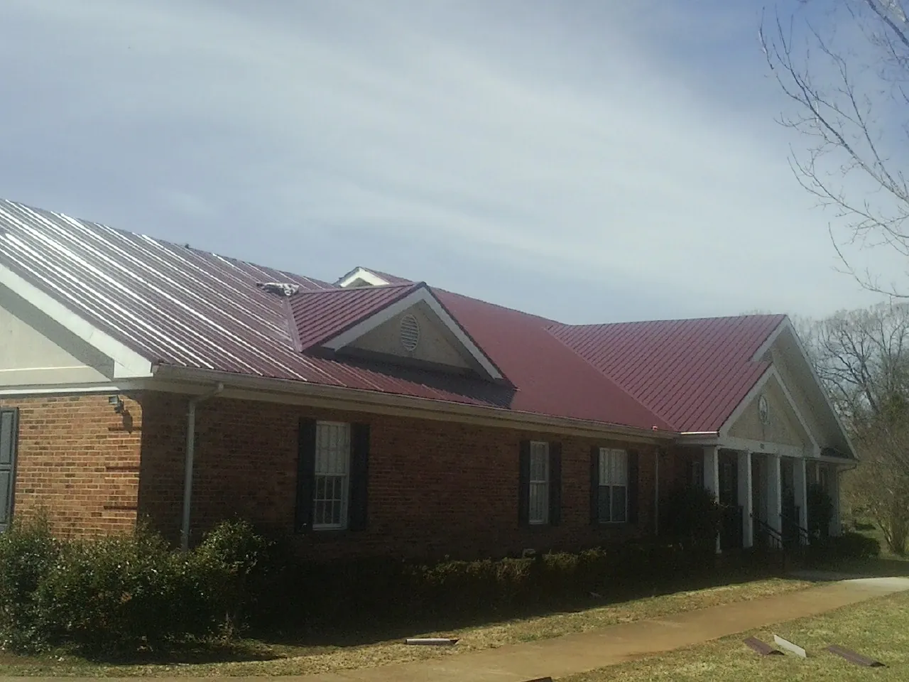 Red metal roof with gabled entries on a long brick building, from a Hail Damage Roof Repair job in Drayden