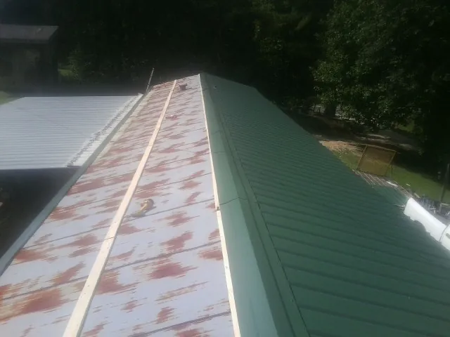Old rusted panels beside newly installed green metal roofing — Wind Damage Roof Repair by Roofing Brothers in Drayden