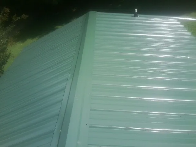New green metal panels meeting at the ridge of a roof — Flat Roof Repair work by our crew in Drayden