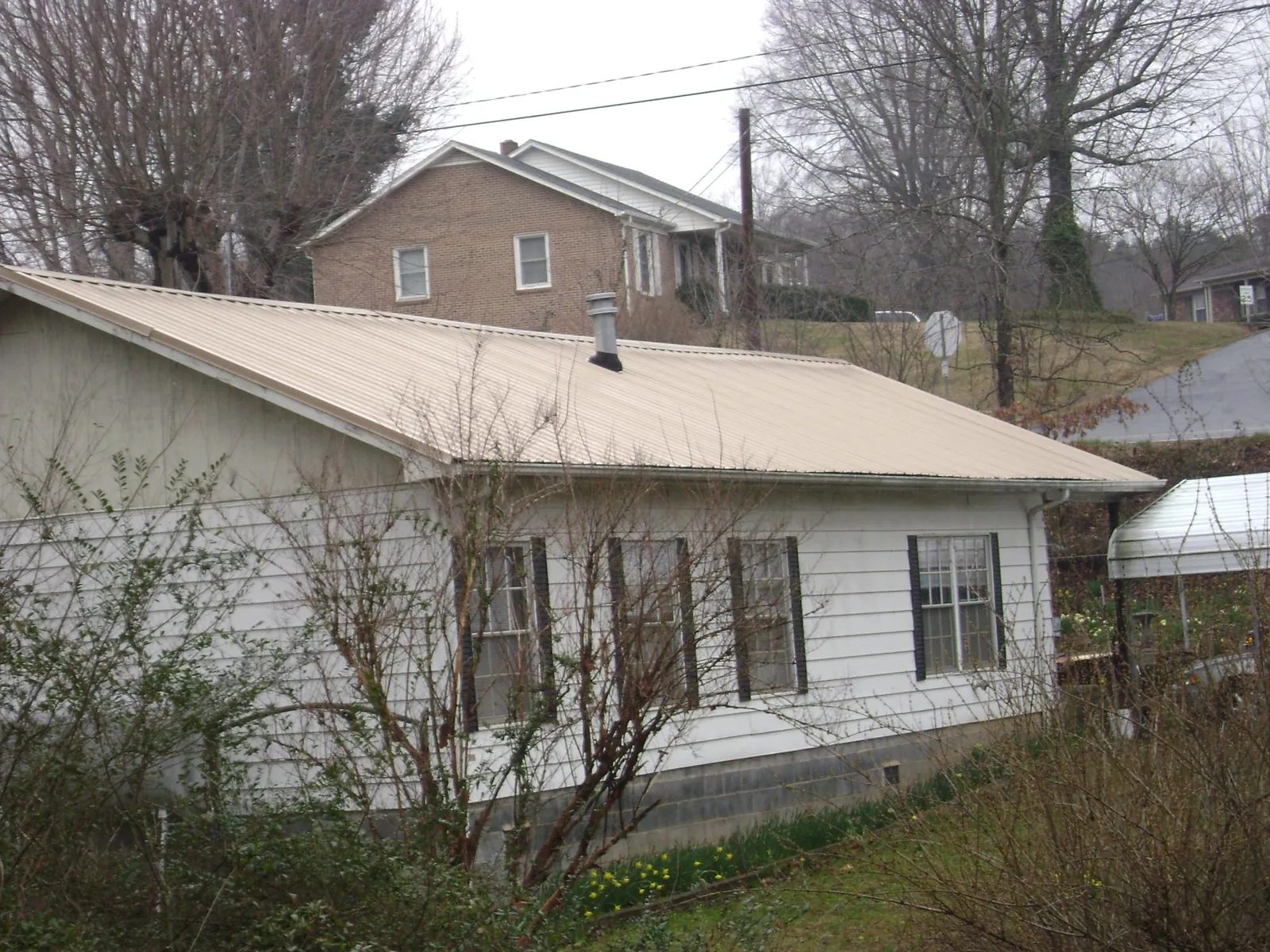Tan metal roof on a white sided house set into a hillside — Commercial Roofing by Roofing Brothers in Drayden